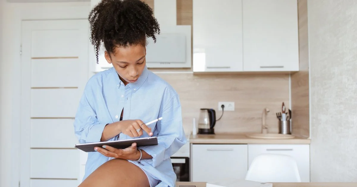 Femme dans la cuisine travaillant sur une tablette avec un stylet, mettant en avant un mode de vie moderne de télétravail.