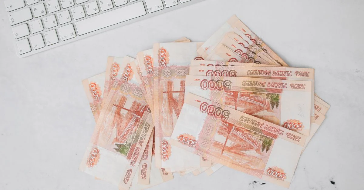 Pile de billets de 5000 roubles à côté d'un clavier sur une surface blanche, vue de dessus.