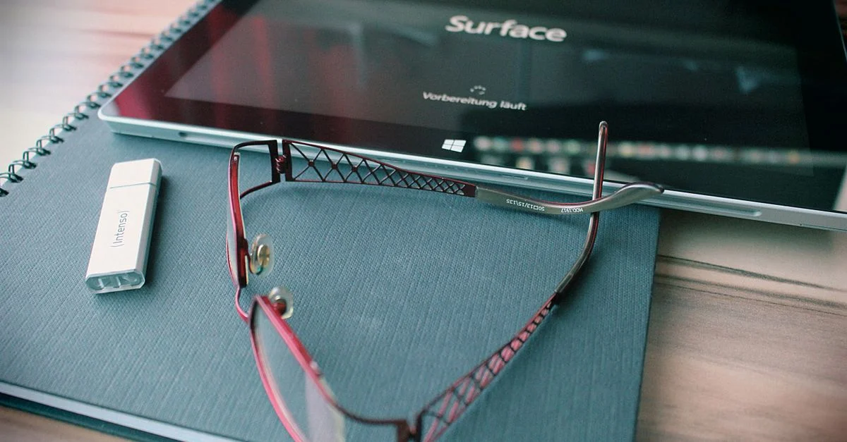Espace de travail organisé avec une tablette, des lunettes et une clé USB sur un bureau.