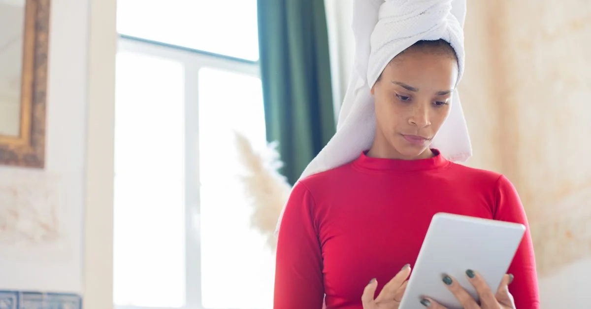 Femme afro-américaine avec une serviette autour de la tête, utilisant une tablette à l'intérieur.