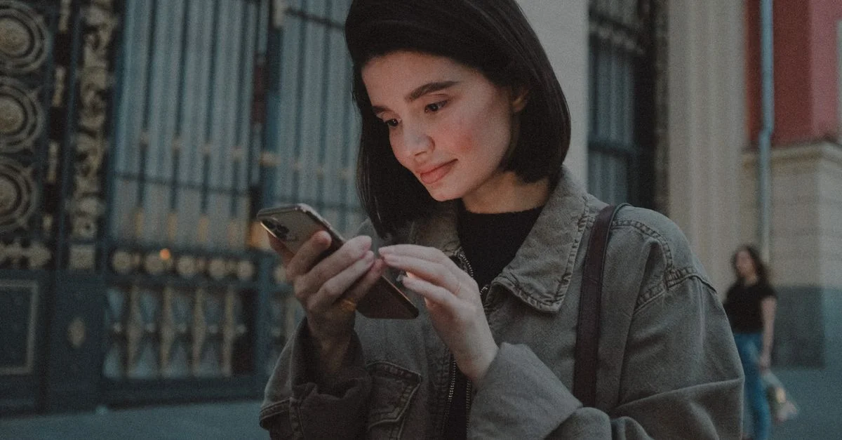Une femme jeune interagissant avec son smartphone à l'extérieur, capturant l'ambiance urbaine d'une soirée.