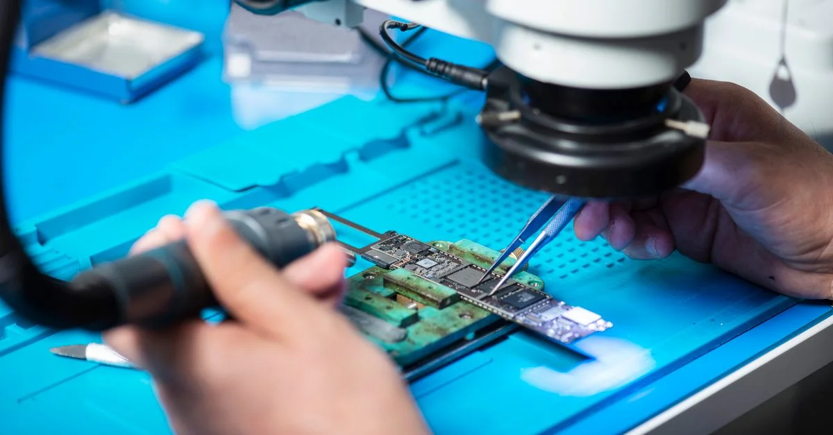 Gros plan d'un technicien réparant un circuit électronique sous un microscope dans un laboratoire à Toronto.
