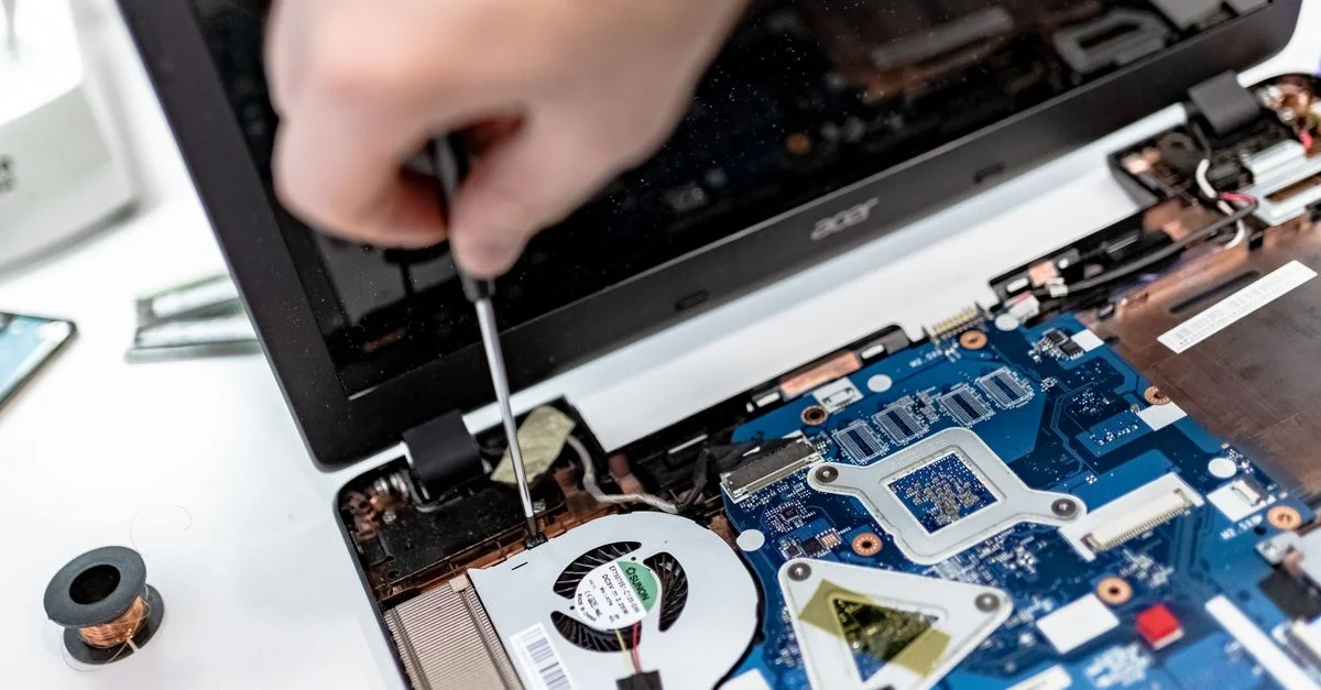 Technicien réparant une carte mère d'ordinateur portable, se concentrant sur les composants électroniques.